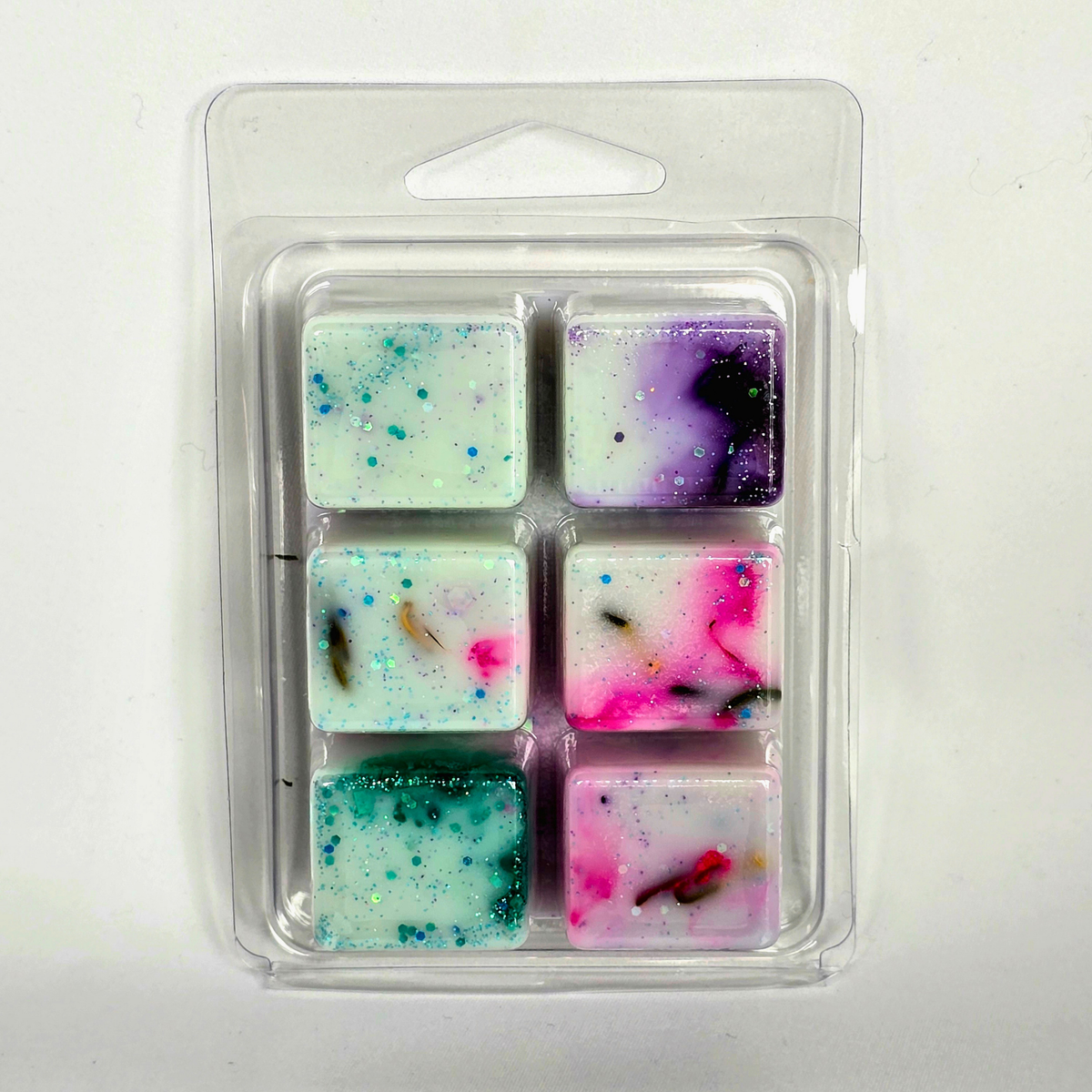 Six square wax melts in a clear plastic clamshell package, each with colorful glitter and embedded natural elements like bark and leaves, on a white background.