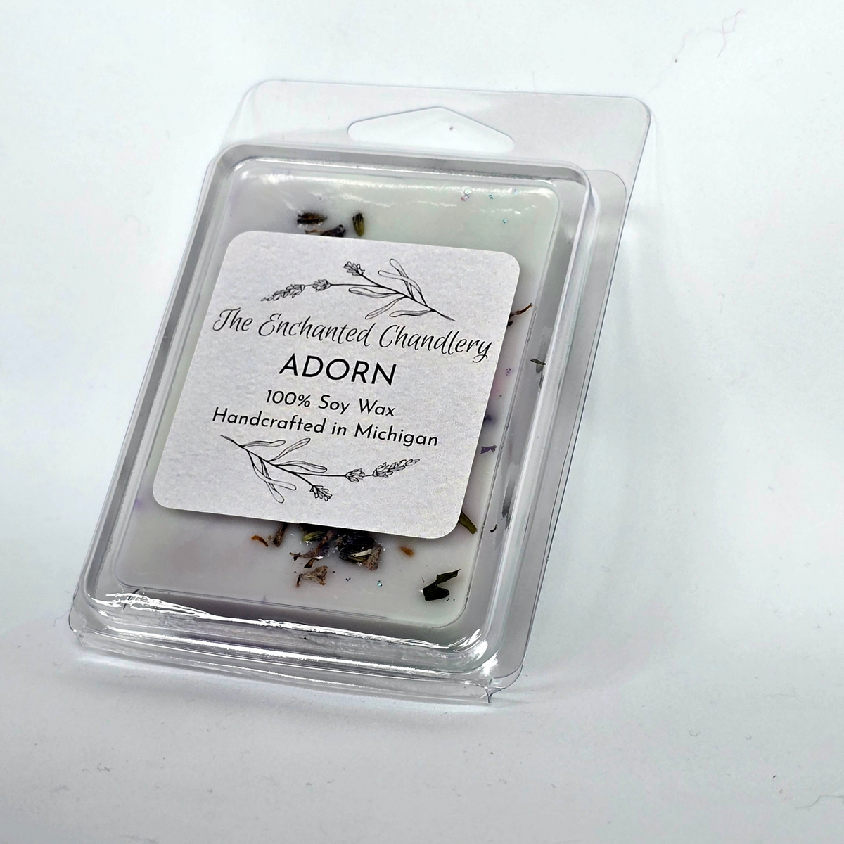 A pale blue packaged soy wax melt in a clear clamshell container with a white label reading 'The Enchanted Chandlery ADORN 100% Soy Wax Handcrafted in Michigan' on a plain white background.