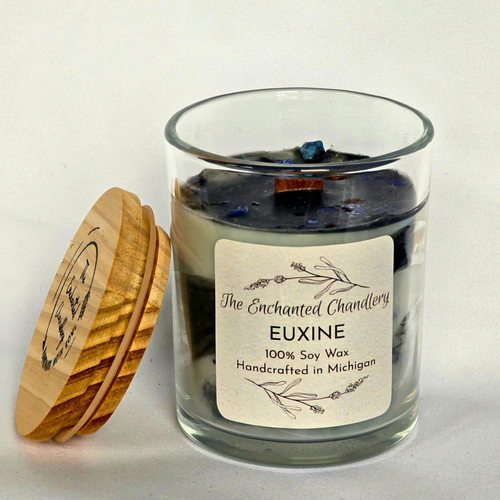A glass jar candle labeled 'The Enchanted Chandlery EUXINE 100% Soy Wax' with a cream label and a wooden lid leaning against it on a light neutral background.