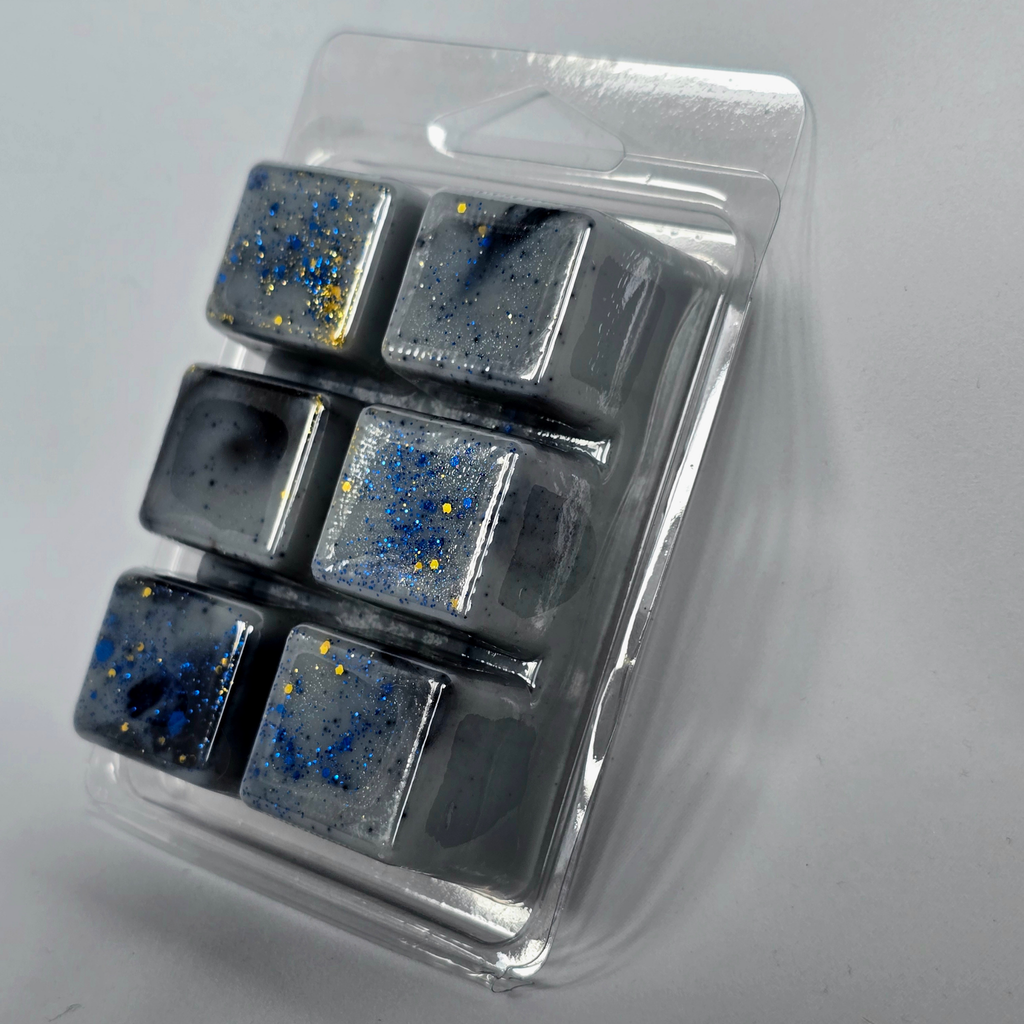 Six square wax melts in a clear plastic container, featuring a dark gray and black space-themed design with blue and gold glitter speckles.