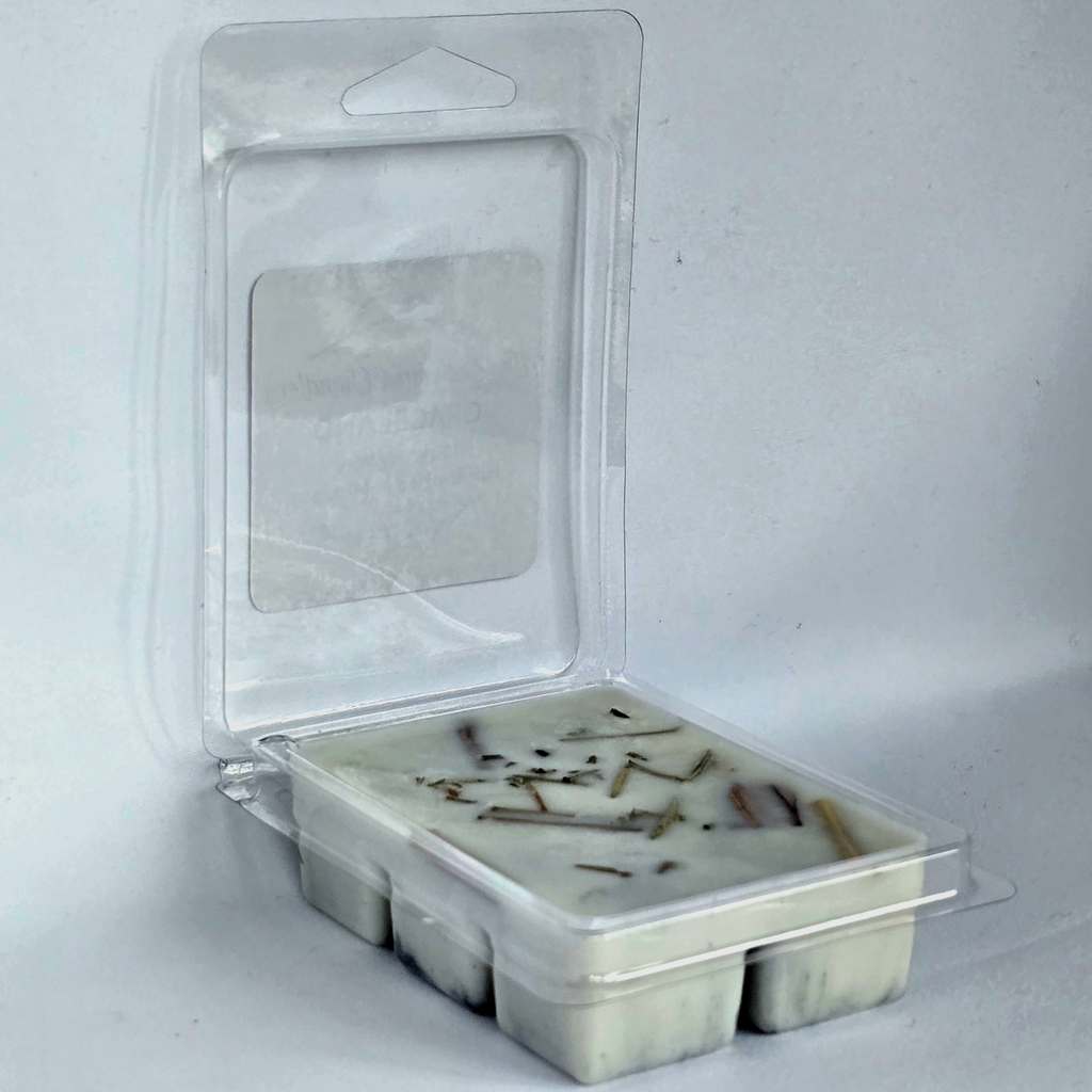 A clear plastic clamshell package containing a white wax melt with small brown botanical inclusions, photographed against a plain light gray background.