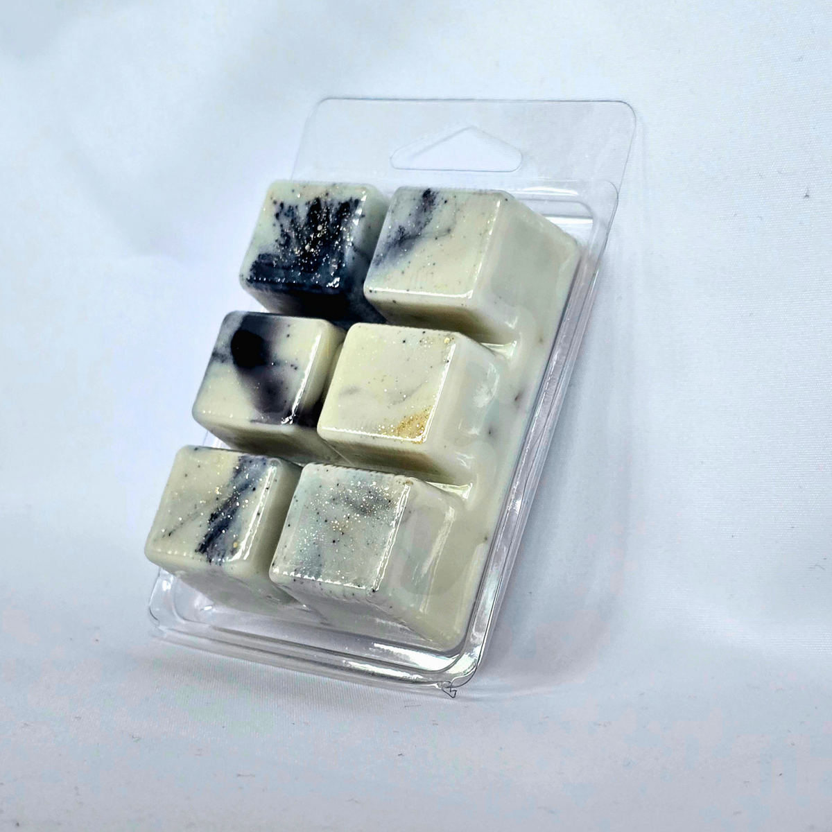 Six square wax melts in a clear plastic clamshell package, featuring a creamy off-white color with black and gold flecks, set against a plain white background.