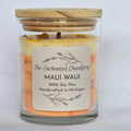 A glass jar candle with a light wood lid, filled with layered yellow and orange wax. A cream-colored paper label on the front reads 'The Enchanted Chandlery', 'MAUI WAUI', and '100% Soy Wax Handcrafted in Michigan'.