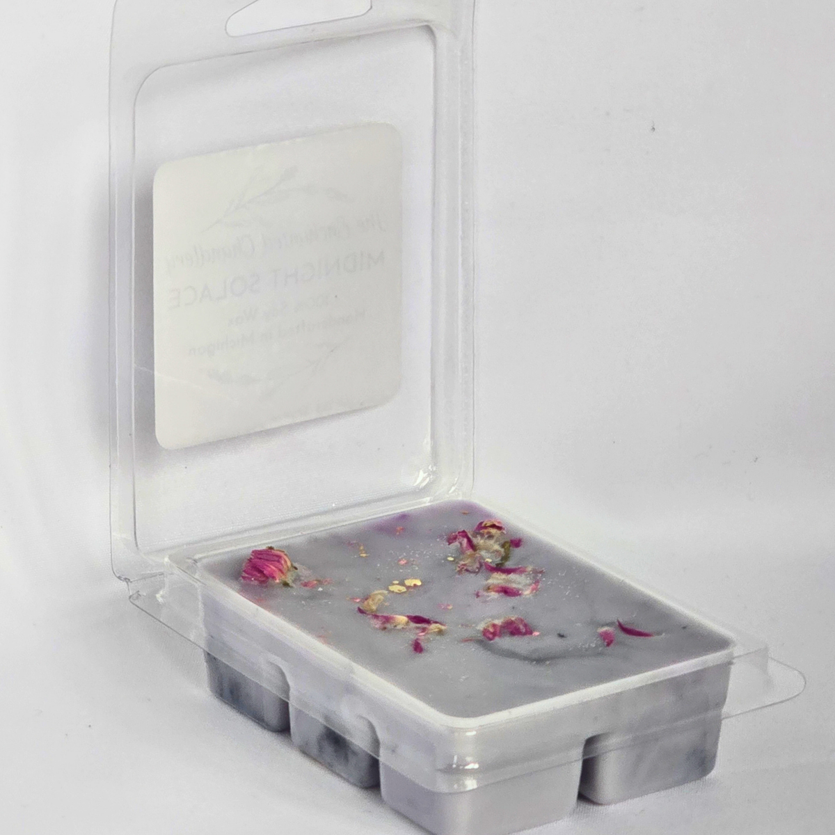 A clear plastic clamshell package containing a rectangular gray marbled wax melt or soap bar with pink dried flower petals on top, photographed on a white background.