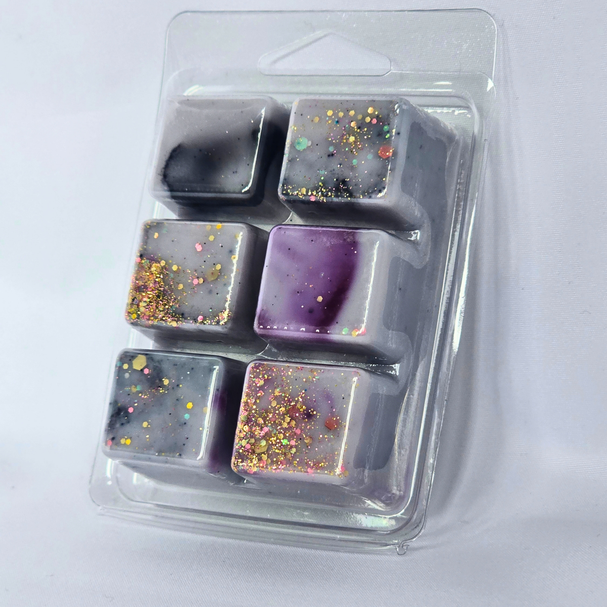 Six square decorative wax melts or soap cubes in a clear plastic clamshell package, featuring marbled gray, purple, and black patterns with gold glitter accents.