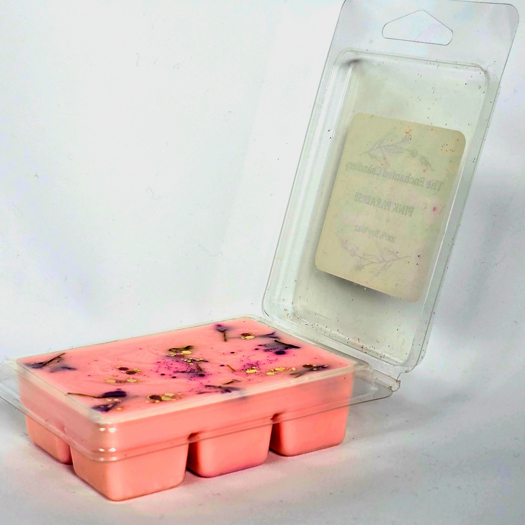 A pink wax melt or soap melt in a clear plastic tray. The wax contains small dried botanical inclusions.