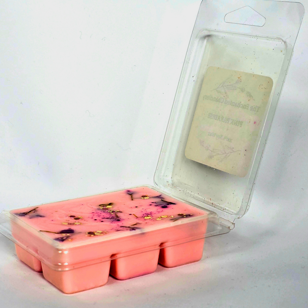 A pink wax melt or soap melt in a clear plastic tray. The wax contains small dried botanical inclusions.