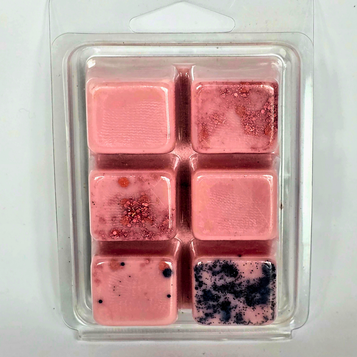Six pink wax melts in a clear plastic clamshell package, featuring various decorative patterns including glitter, flecks, and dark speckles.
